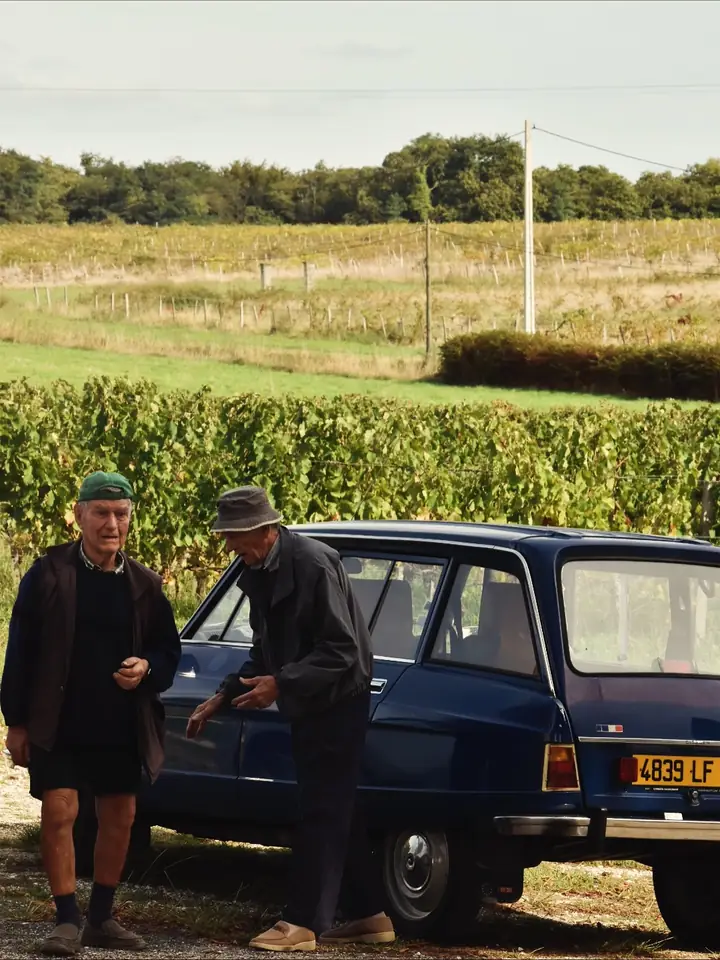 Deux anciens discutent devant une Citroën, les vignes en arrière-plan